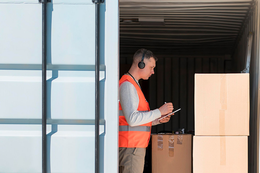 Inside a shipping container, a man wearing an orange vest demonstrates the use of Conex boxes for storage.