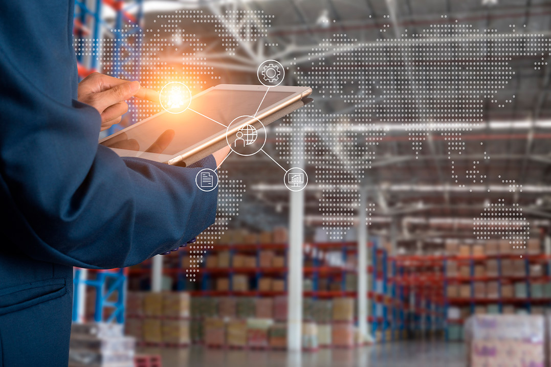 A warehouse employee operates a tablet, overseeing stock management in a busy warehouse environment.