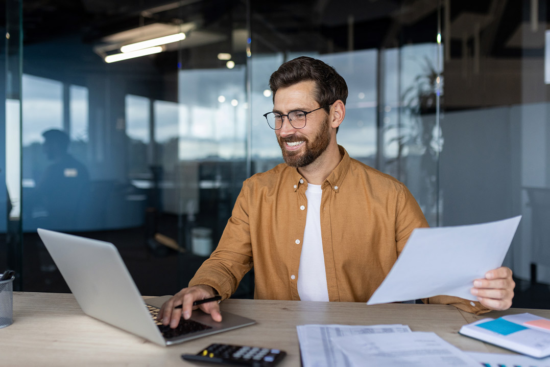 A bearded man wearing glasses is seated at a desk with a laptop, focused on bonded warehousing solutions for Texas companies.