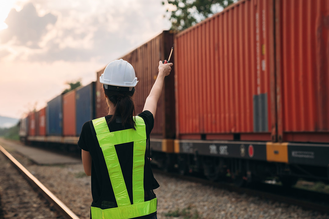 A woman wearing a hard hat gestures towards a train, emphasizing shipping containers available in South Texas.