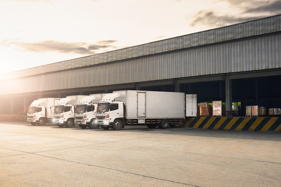 A lineup of three white trucks stationed outside a warehouse, highlighting the industrial setting.