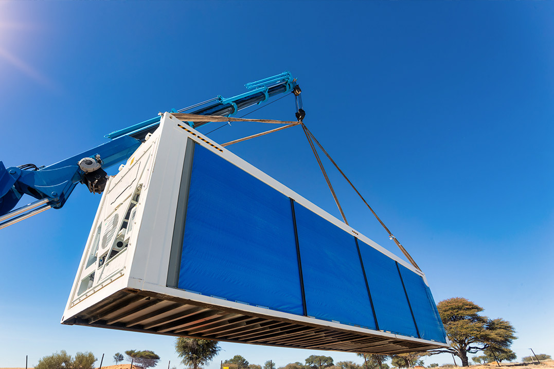 A crane hoists a container into the air under a bright blue sky, representing the start of the spring construction season.