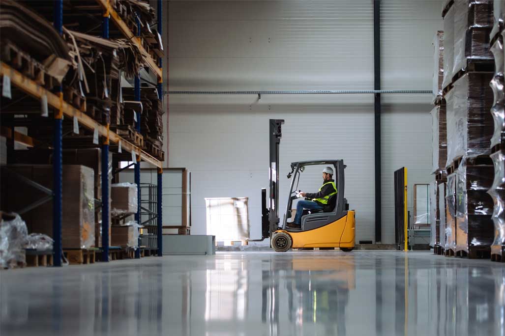 Side view of forklift in warehouse with male driver. Warehouse worker preparing products for shipmennt, delivery, checking stock in warehouse.