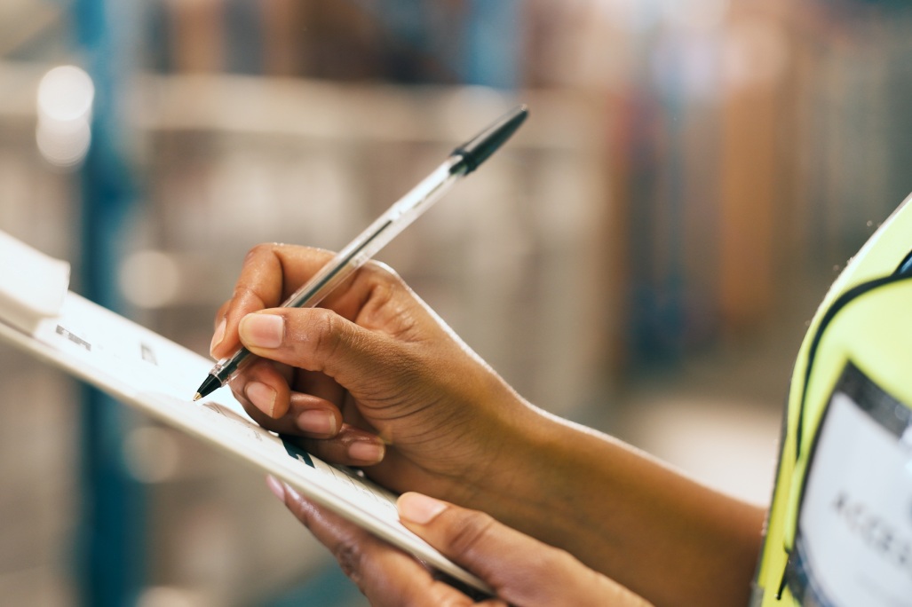 Logistics, writing and hands with clipboard in warehouse, supply chain and quality assurance report. Factory, notes and person with checklist for stock distribution, shipping or inspection for export